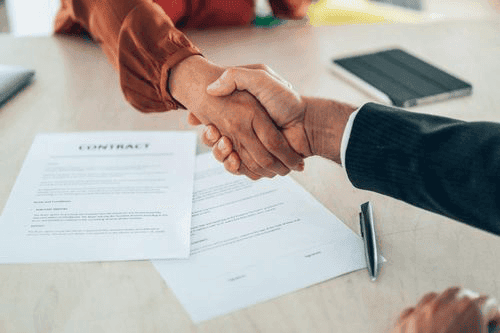Two people shake hands over a signed contract, representing the successful conclusion of an auto title loan contract